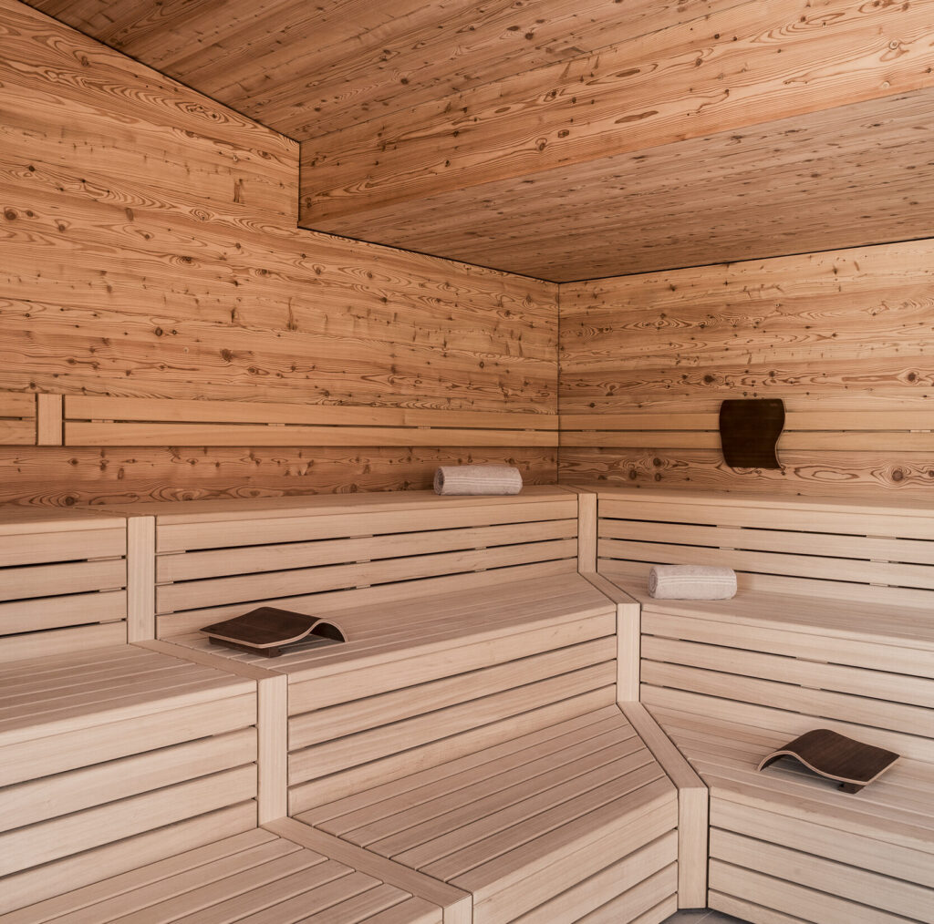 Interior of a Finnish sauna with wooden benches, walls, and ceiling. Towels and headrests are neatly arranged.