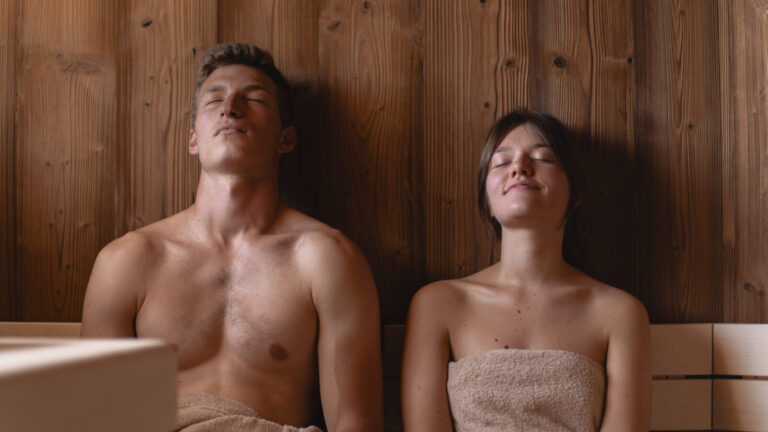 Relaxed couple sitting in a wooden sauna wrapped in towels