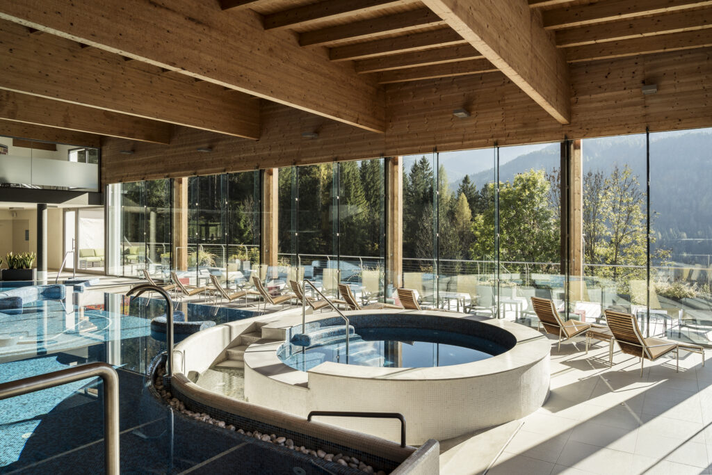 Indoor spa with pool, hot tub, and lounge chairs at Day Spa Cadore Dolomiti, showcasing relaxation and mountain views.
